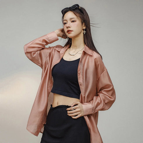 Woman wearing a pink satin shirt over a black top and pants on a neutral background